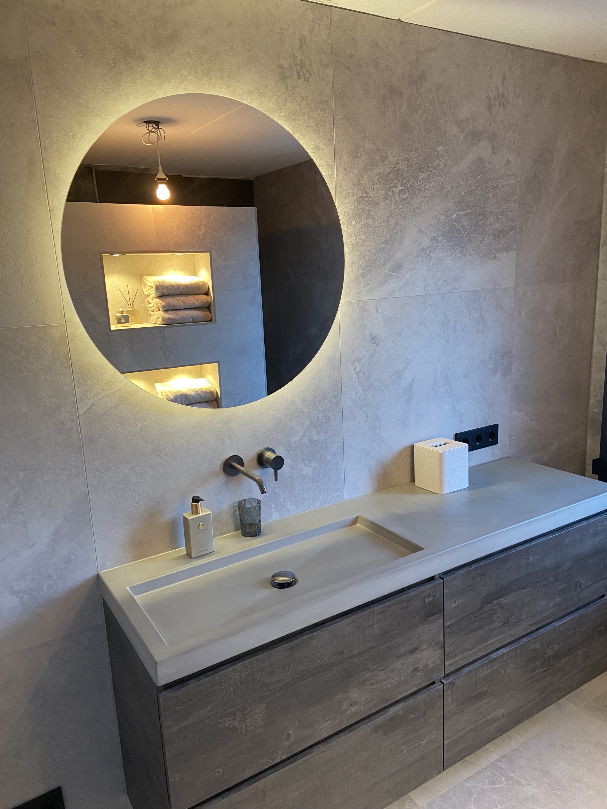 Badkamer met een ronde lichtspiegel en betonlook tegels